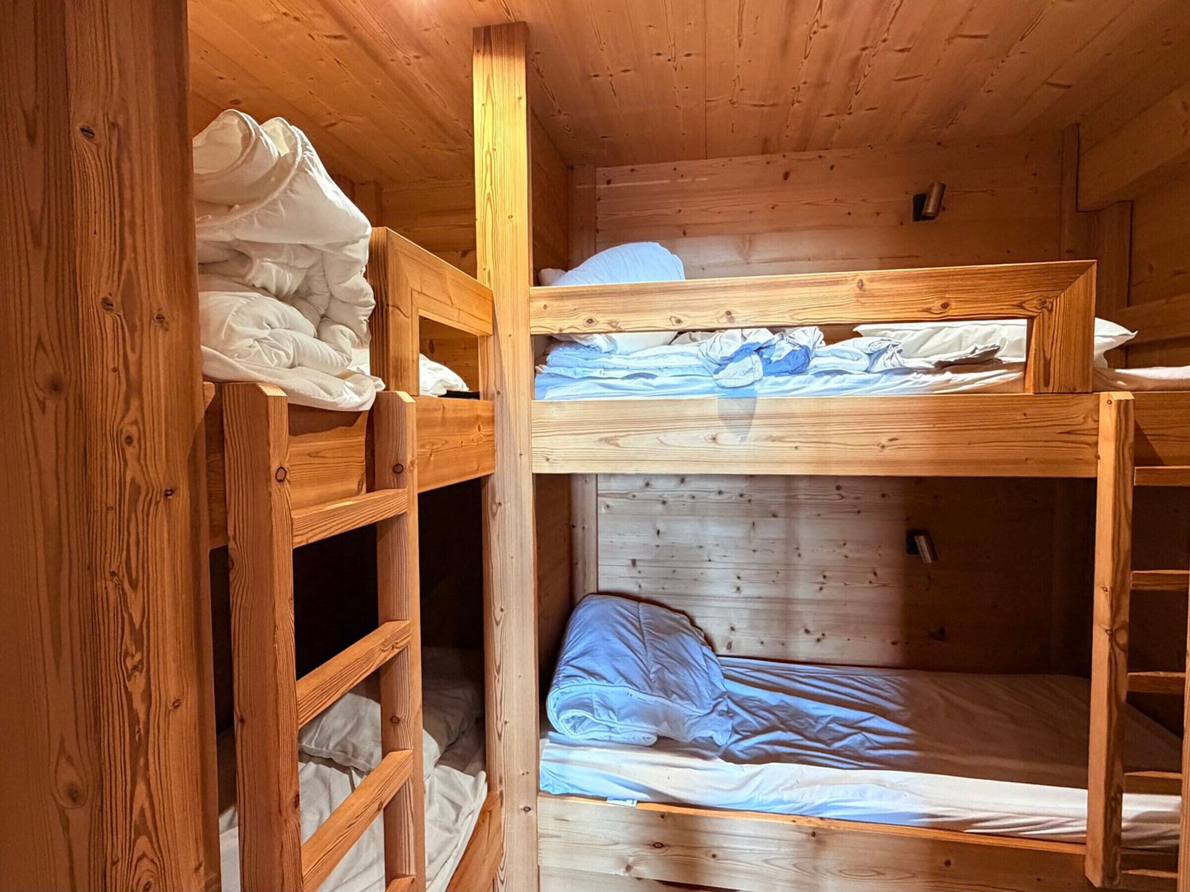 A wooden bunk bed room with a ladder and a small shelf.