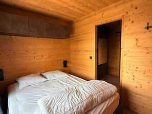 A wooden cabin room with a bed, a small table, and a door leading to another room. - Contemporary chalet apartment - 8 guests (Chamrousse)