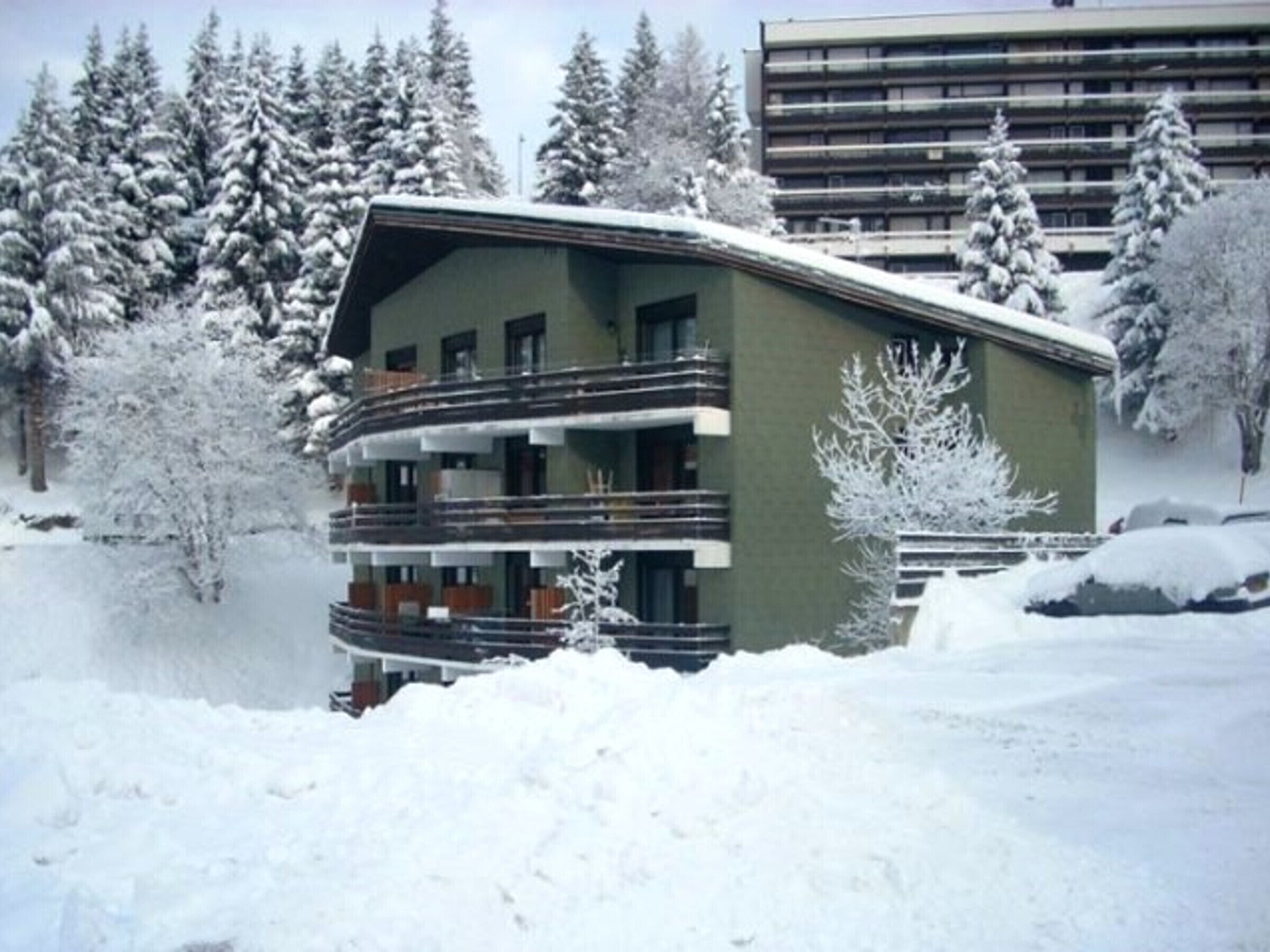 A multi-story building with balconies, surrounded by snow-covered trees.