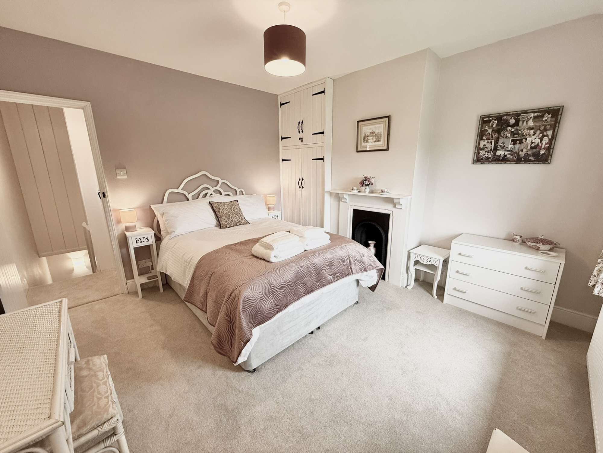 A bedroom with a bed, bedside tables, a dresser, a fireplace, and a wall-mounted picture.