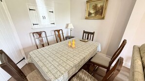 A dining room with a patterned tablecloth, wooden chairs, a table lamp, and a framed picture on the wall. - Yew Tree Cottage – Direct New Forest Access, Ponies & Walk to Lyndhurst (Lyndhurst)