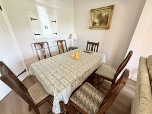 A dining room with a patterned tablecloth, wooden chairs, a table lamp, and a framed picture on the wall. - Yew Tree Cottage – Direct New Forest Access, Ponies & Walk to Lyndhurst (Lyndhurst)
