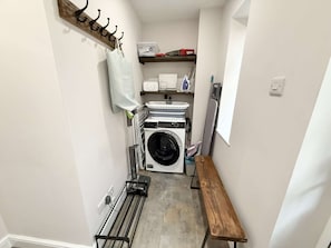 A laundry room with a washing machine, dryer, ironing board, and a bench. - Yew Tree Cottage – Direct New Forest Access, Ponies & Walk to Lyndhurst (Lyndhurst)