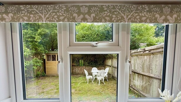 A window with a view of a garden, a wooden fence, and a white table with chairs. - Yew Tree Cottage – Direct New Forest Access, Ponies & Walk to Lyndhurst (Lyndhurst)
