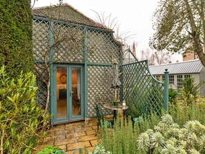 A house with a green lattice fence, a wooden door, and a small table with a chair. - Countryside Barn Near River Great Ouse (Huntingdon)