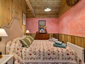 A bedroom with a wooden ceiling, a bed with floral bedding, a dresser, and a radiator. - Countryside Barn Near River Great Ouse (Huntingdon)