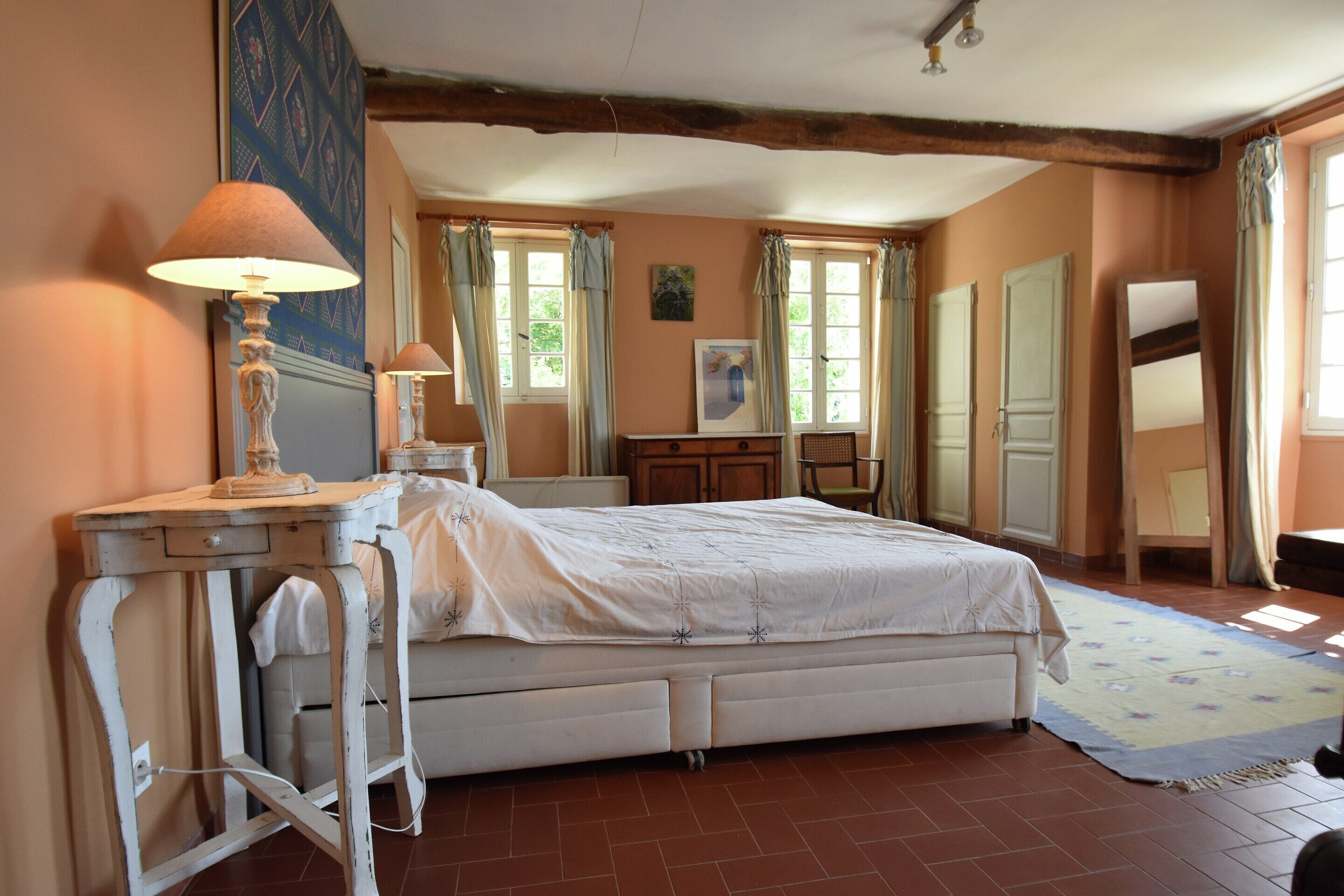 A bedroom with a bed, bedside tables, a dresser, a mirror, and a window with curtains.