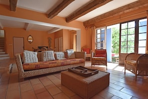 A spacious living room with a large sofa, wicker chairs, and a dining area in the background. - Large Holiday Home With a Swimming Pool in Le Var (Collobrieres)