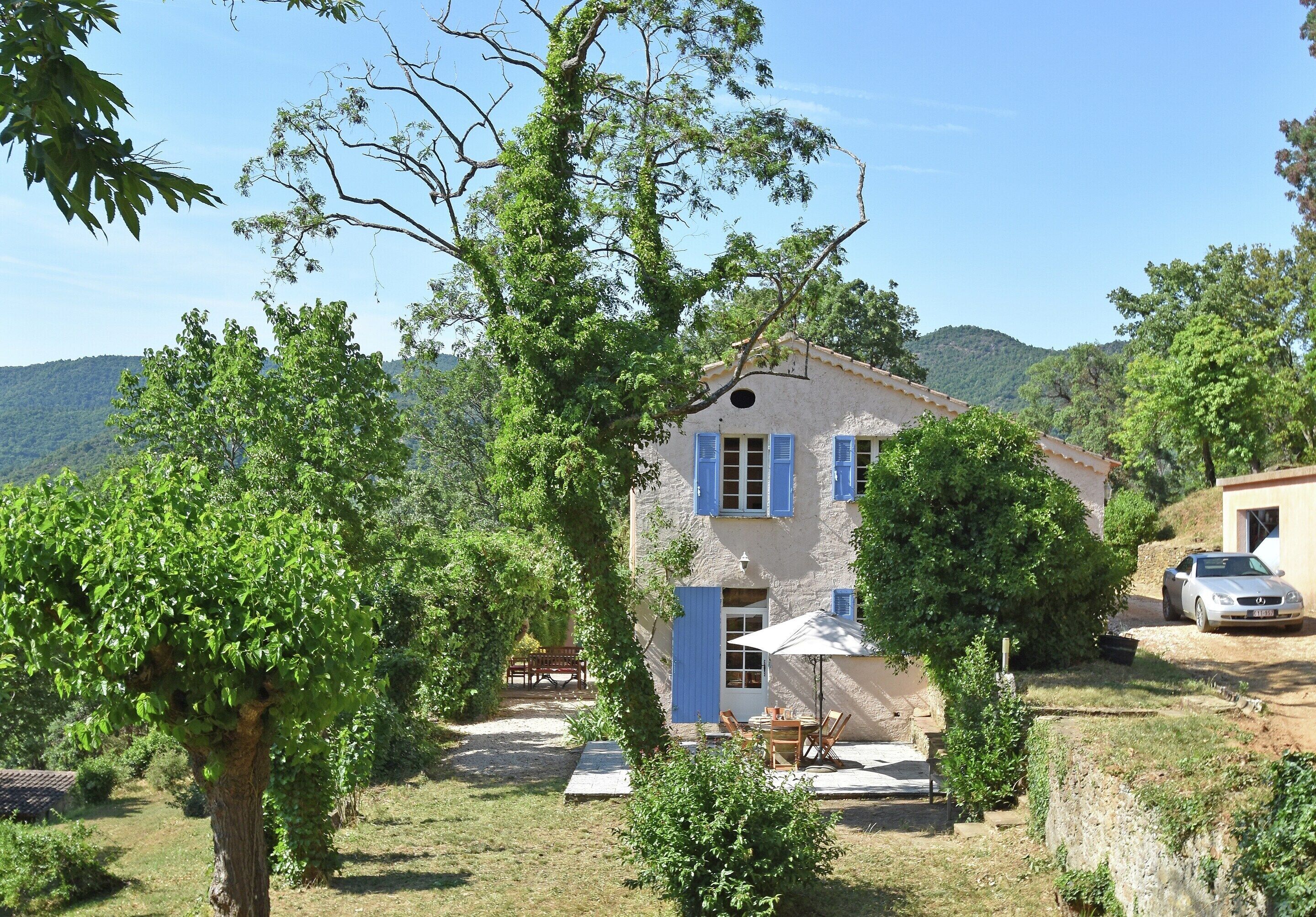 Une maison à deux étages avec un jardin, un coin repas aménagé avec du mobilier d’extérieur et une voiture garée.