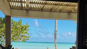 A dining area with a view of the beach, a palm tree, and a person walking on the shore. - Room-luxury Hacienda Residence Punta Can (Punta Cana)