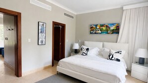 A bedroom with a bed, bedside tables, a painting, a door, and a window. - Room-luxury Hacienda Residence Punta Can (Punta Cana)