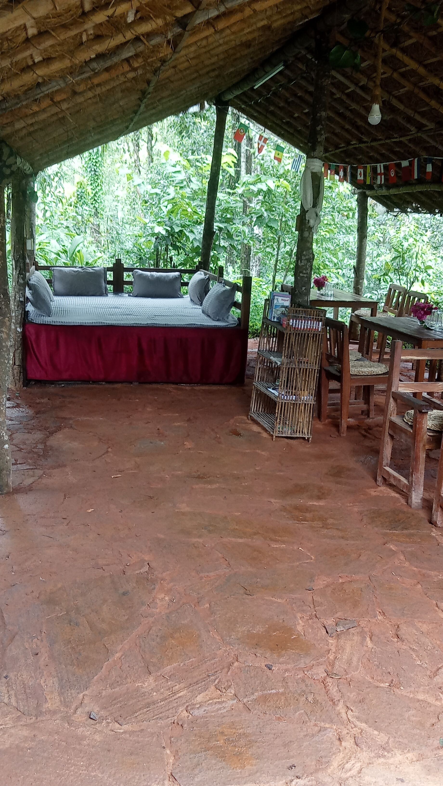 Un área de estar al aire libre con una mesa y sillas cubiertas, rodeada de abundante vegetación.