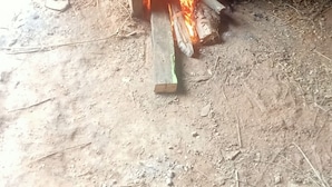Een metalen pot boven een open vuur, met brandhout dat op de grond smeult.