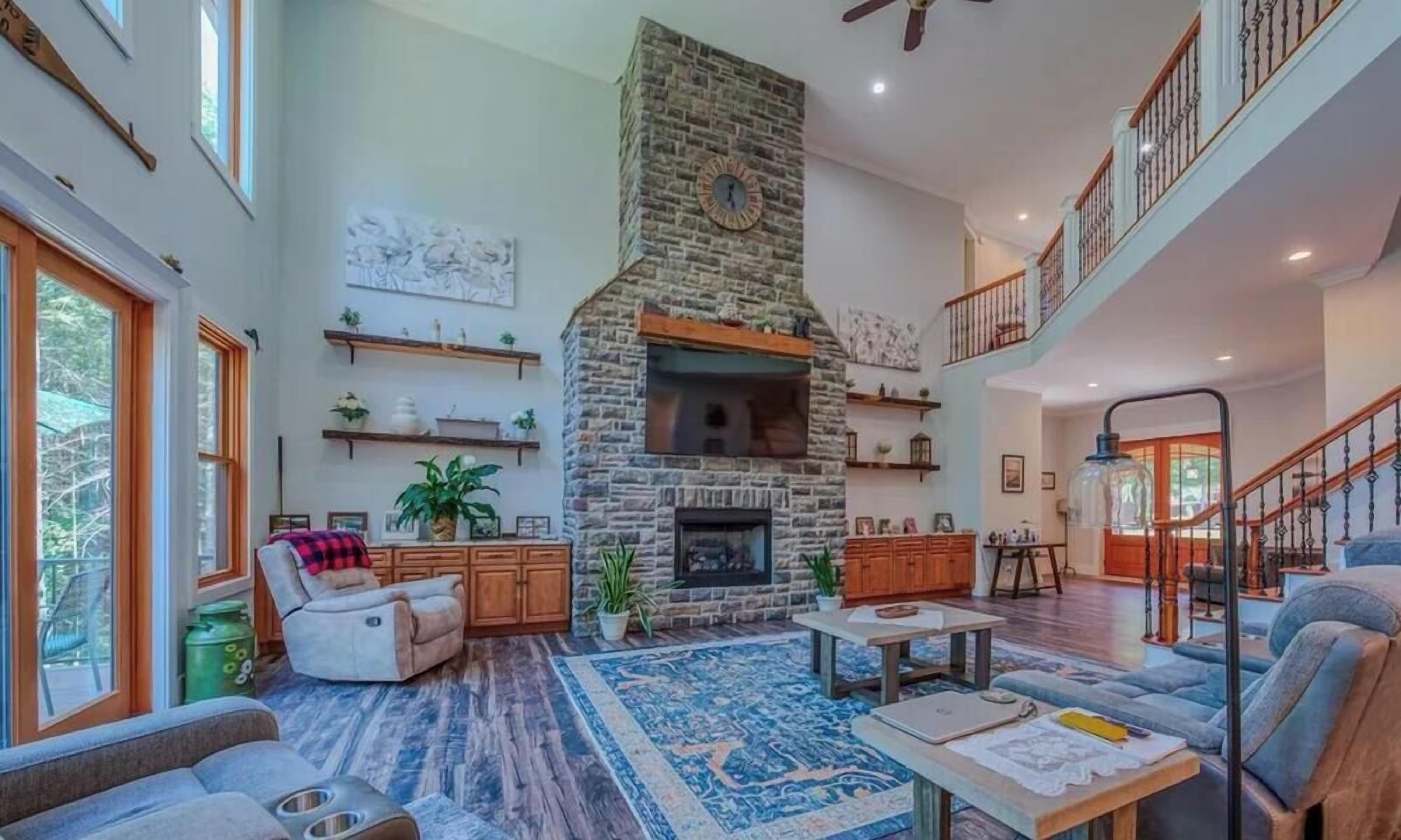 A spacious living area with a stone fireplace, a balcony, and a staircase.