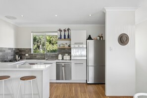 A modern kitchen with a central island, stainless steel appliances, and a view of greenery outside. - Coastal living in beautiful Cottesloe (Cottesloe)