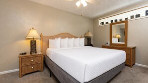 Un dormitorio ordenado con cama, dos mesitas de noche, un velador, ventilador de techo y un espejo grande.