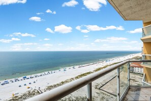 A beach view from a balcony with a clear sky, a pier in the distance, and beach umbrellas. - 🏖️ Emerald Isle 1402 | 14th Floor Beachfront | 2 Pools + Walk to Pier (Gulf Breeze)