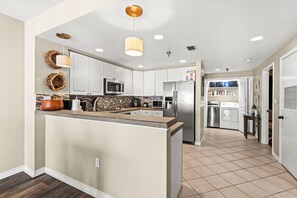 A modern kitchen with white cabinets, stainless steel appliances, and a central island. - 🏖️ Emerald Isle 1402 | 14th Floor Beachfront | 2 Pools + Walk to Pier (Gulf Breeze)