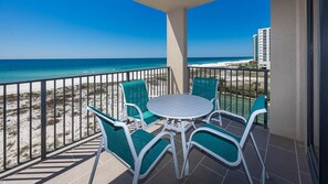 Un balcon avec une table et des chaises, donnant sur une plage et l’océan.