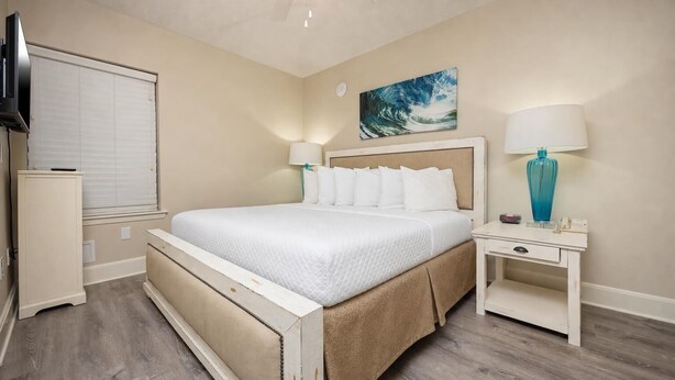 A bedroom with a bed, bedside tables, a TV, and a painting on the wall. - Phoenix X 502 1 Bedroom Condo (Orange Beach)