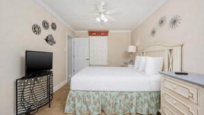A hotel room with a bed, a television on a stand, a ceiling fan, and a door. - Phoenix Iii 3096 2 Bedroom Condo (Orange Beach)
