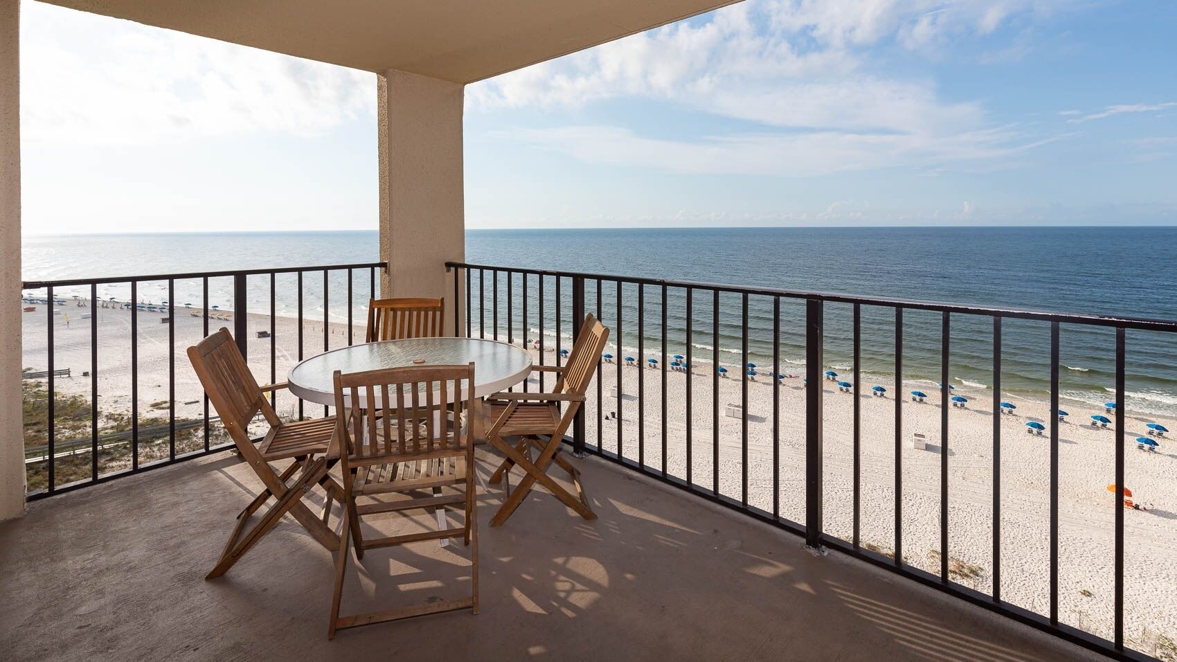 A balcony with a table and chairs overlooking a beach.