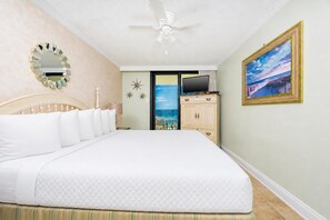 Ein Hotelzimmer mit einem Bett, einem Fernseher, einem Gemälde und Blick aufs Meer durch eine Tür.