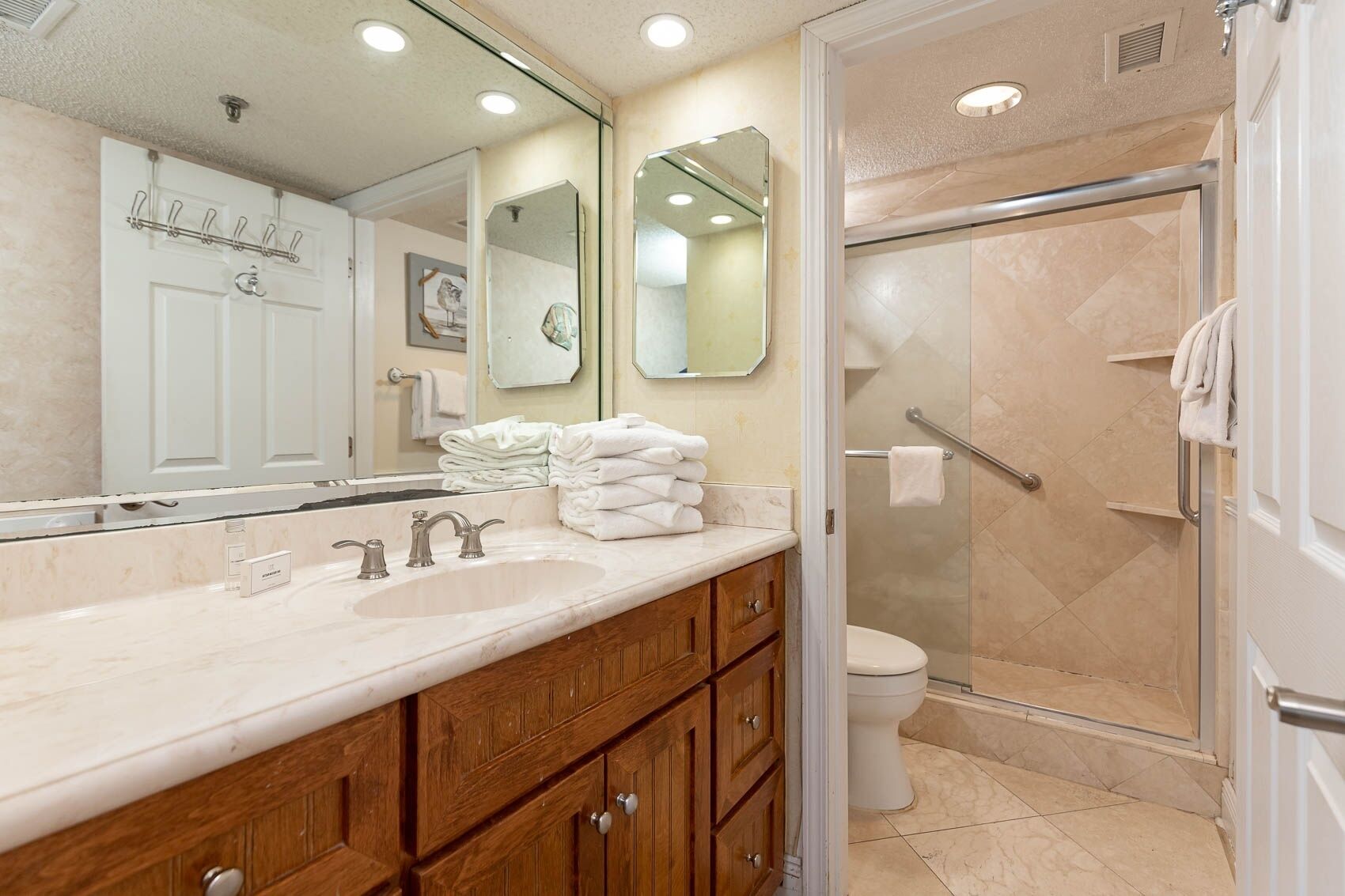 A bathroom with a marble sink, wooden cabinets, a glass shower enclosure, and a white toilet.