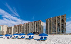 A beachfront hotel with multiple high-rise buildings, beach umbrellas, and sun loungers. - Phoenix Iii 3053 1 Bedroom Condo (Orange Beach)