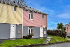 A two-story residential building with a grey and pink facade, white doors, and a small front yard with grass and a tree. - Spacious Holiday Home in Newquay (St. Columb Major)