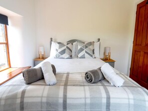 A bed with a plaid bedspread, two pillows with geometric patterns, and two rolled towels. - 3-bedroom Cottage Near Coast (Bude)
