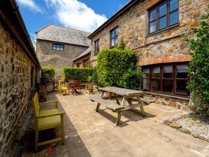 A courtyard with stone buildings, a wooden bench, and a picnic table. - 3-bedroom Cottage Near Coast (Bude)