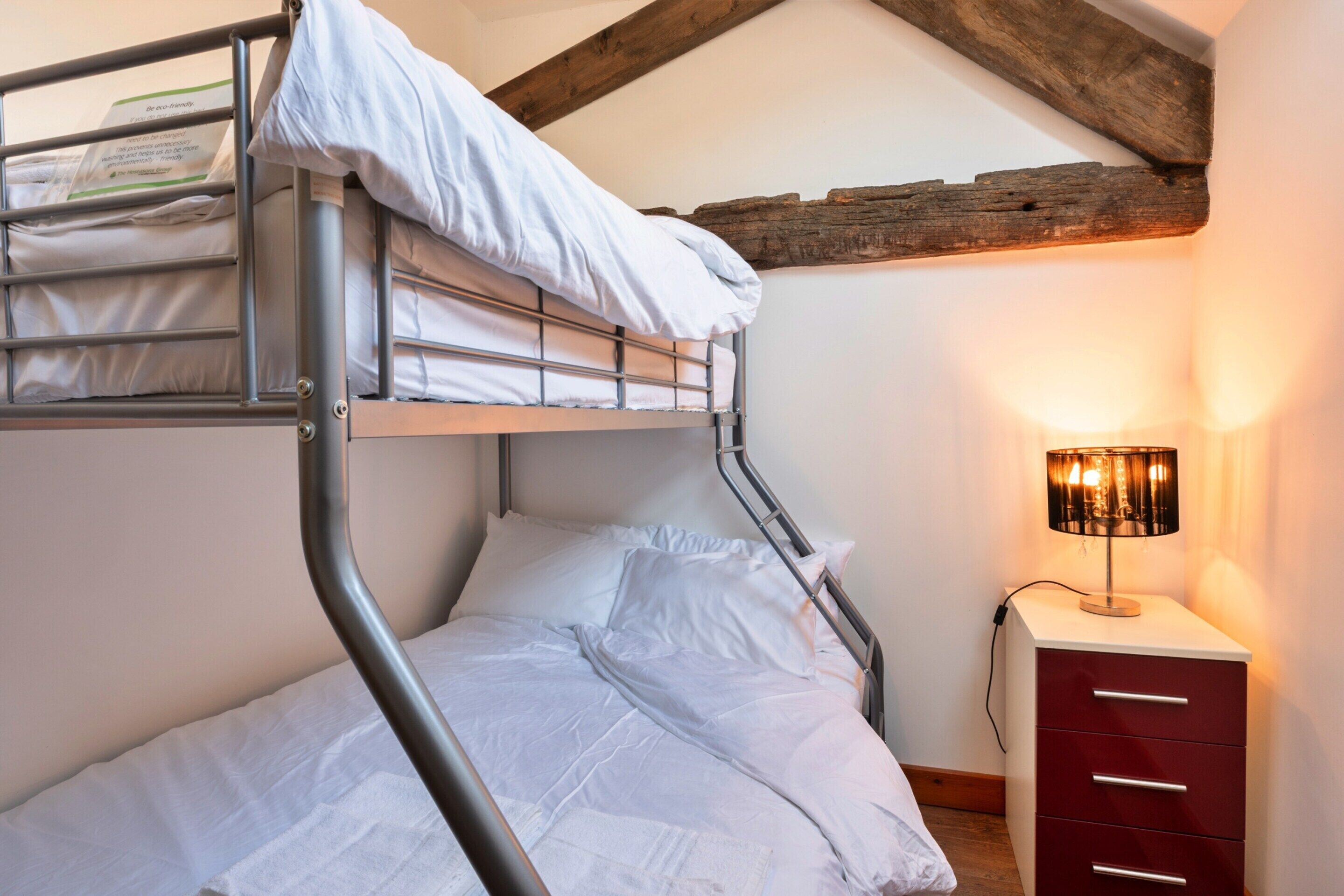 Ein Etagenbett mit Metallgestell, weißer Bettwäsche und einem Nachttisch mit Schubladen.