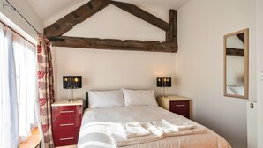 Une chambre à coucher avec un lit, deux tables de chevet, un miroir et une fenêtre avec des rideaux.