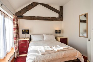A bedroom with a bed, two bedside tables, a mirror, and a window with curtains. - Devon Cottage With Games Room (Exeter)