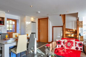 A modern kitchen with white cabinets, a dining area with a table and chairs, and a living room with a red sofa and floral cushions. - Devon Cottage With Games Room (Exeter)