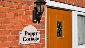 Un mur de briques avec une enseigne indiquant « Poppy Cottage » et une porte traditionnelle dotée d’une fenêtre.