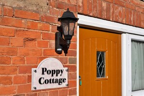 A brick wall with a 'Poppy Cottage' sign and a traditional door with a window. - Devon Cottage With Games Room (Exeter)