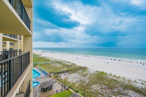 A beach view from a balcony with a pool and lounge chairs.