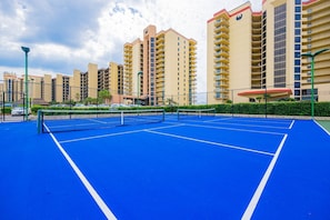 Una cancha de tenis con red, rodeada por una cerca y contigua a edificios residenciales.