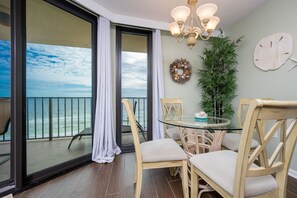 Un balcon avec une porte vitrée donnant sur l’océan, une table ronde en verre avec des chaises, un lustre et une guirlande décorative fixée au mur.