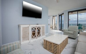 A modern living room with a flat-screen TV, a wooden coffee table, and a sofa. - Phoenix X 608 1 Bedroom Condo (Orange Beach)