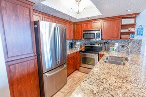 A modern kitchen with stainless steel appliances, wooden cabinets, and a granite countertop. - 705 S Hampton Oceanview Retreat With Balcony 2 Bedroom Condo (Myrtle Beach)