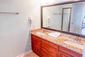 A bathroom with a double sink vanity, a large mirror, and two hair dryers mounted on the wall.