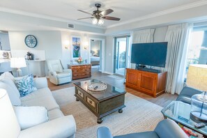Ein geräumiges Wohnzimmer mit Deckenventilator, Flachbildfernseher, Couchtisch und Sofa.