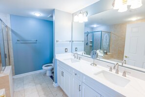 Ein modernes Badezimmer mit barrierefreier Dusche, Toilette, Waschbecken mit großem Spiegel und Handtuchhalter.