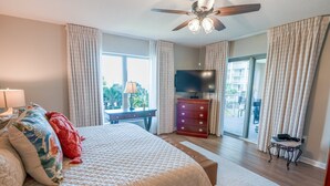 A bedroom with a bed, a dresser, a television, and a balcony with curtains. - 102 Royale Palms Oceanfront 2br Resort Access 2 Bedroom Condo (Myrtle Beach)