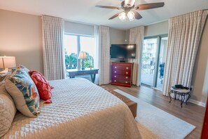 Ein Schlafzimmer mit Bett, Kommode, Fernseher und einem Balkon mit Vorhängen.