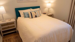 A neatly made bed with a teal headboard, white bedding, and two bedside lamps on matching nightstands. - Pelican Beach 1013 2 Bedroom Condo (Destin)