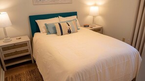 A neatly made bed with a teal headboard, white bedding, and two bedside lamps on matching nightstands. - Pelican Beach 1013 2 Bedroom Condo (Destin)
